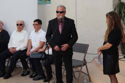 Predsednik društva Janez Kermc v temni obleki in s sončnimi očali govori za mikrofonom.